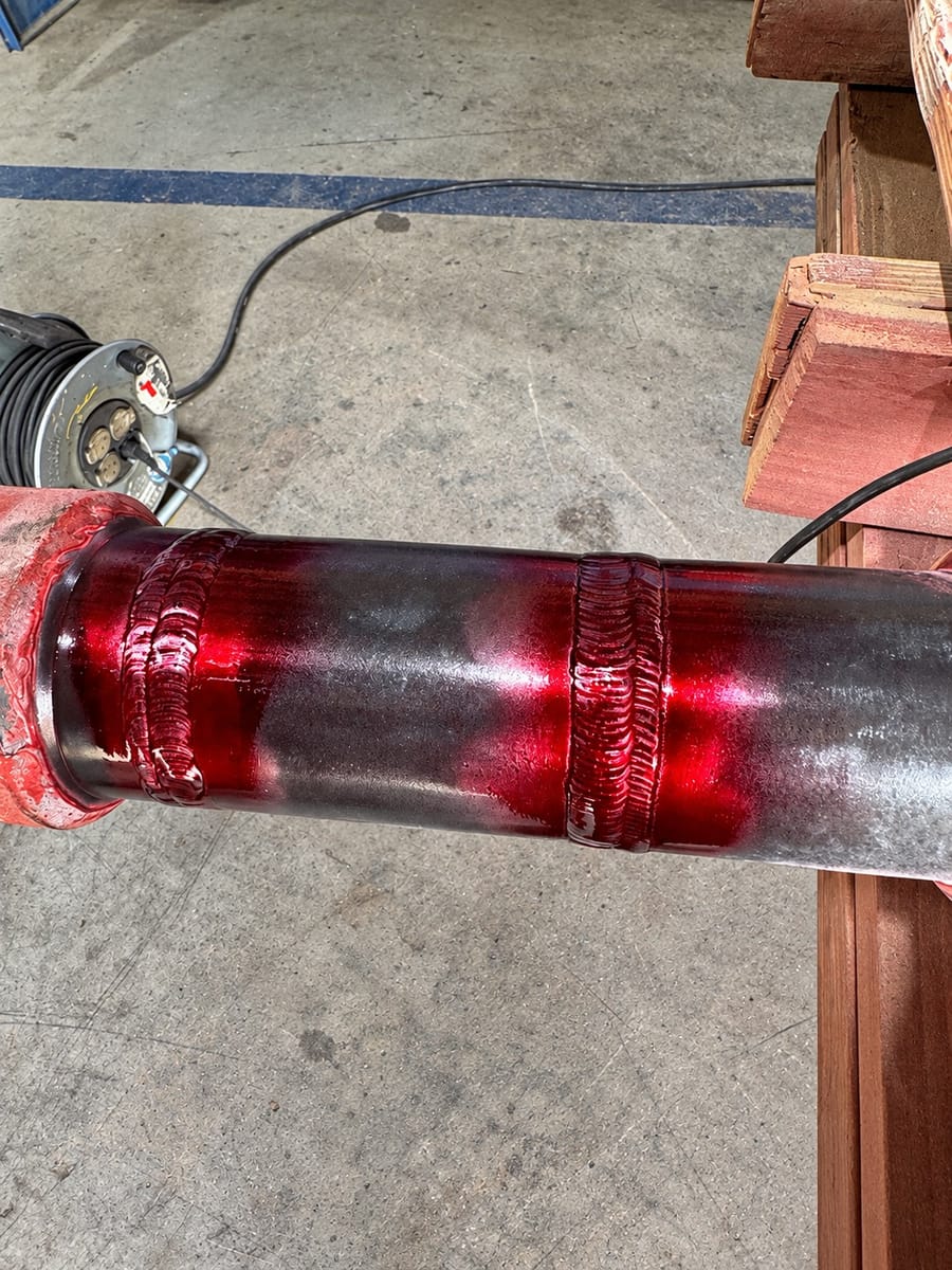 Red dye penetrant applied over two circumferential welds on a flanged pipe spool.